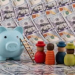 A Group Of Symbolic Wooden People Against A Background Of $100 Bills.